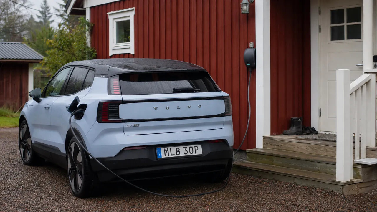 Volvo EX30 laddas vid ett rödmålat trähus en mulen morgon.