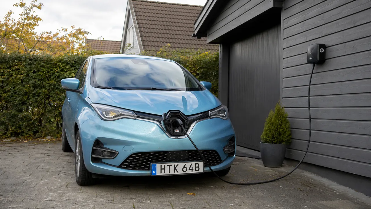 Blå Renault Zoe laddar från en laddbox vid ett grått garage.