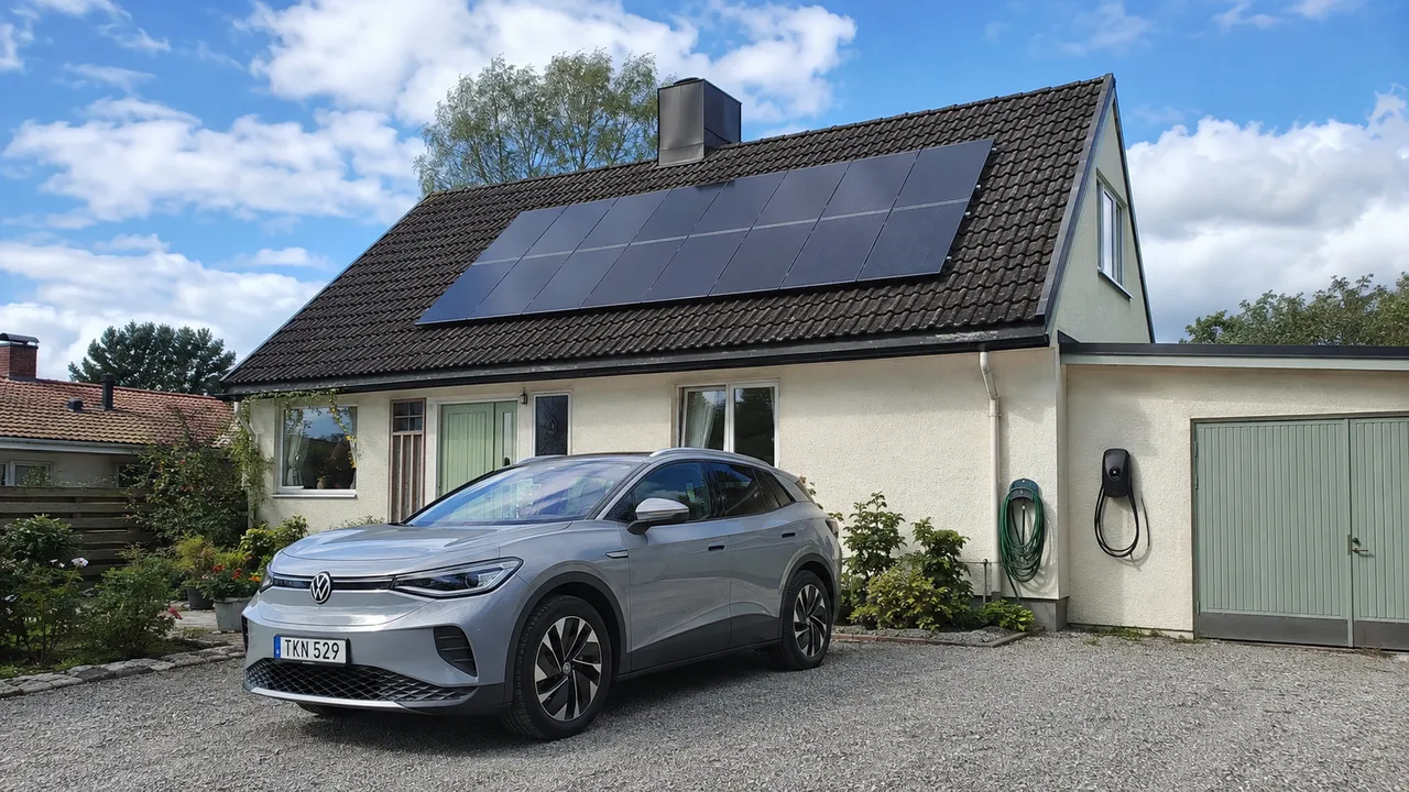 Villa med solpaneler på taket, elbil på grusuppfarten och laddbox på garageväggen.