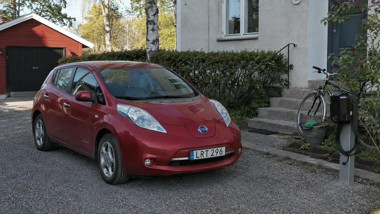 Röd Nissan Leaf vid en putsad villa med en laddbox på stolpe bredvid uppfarten.