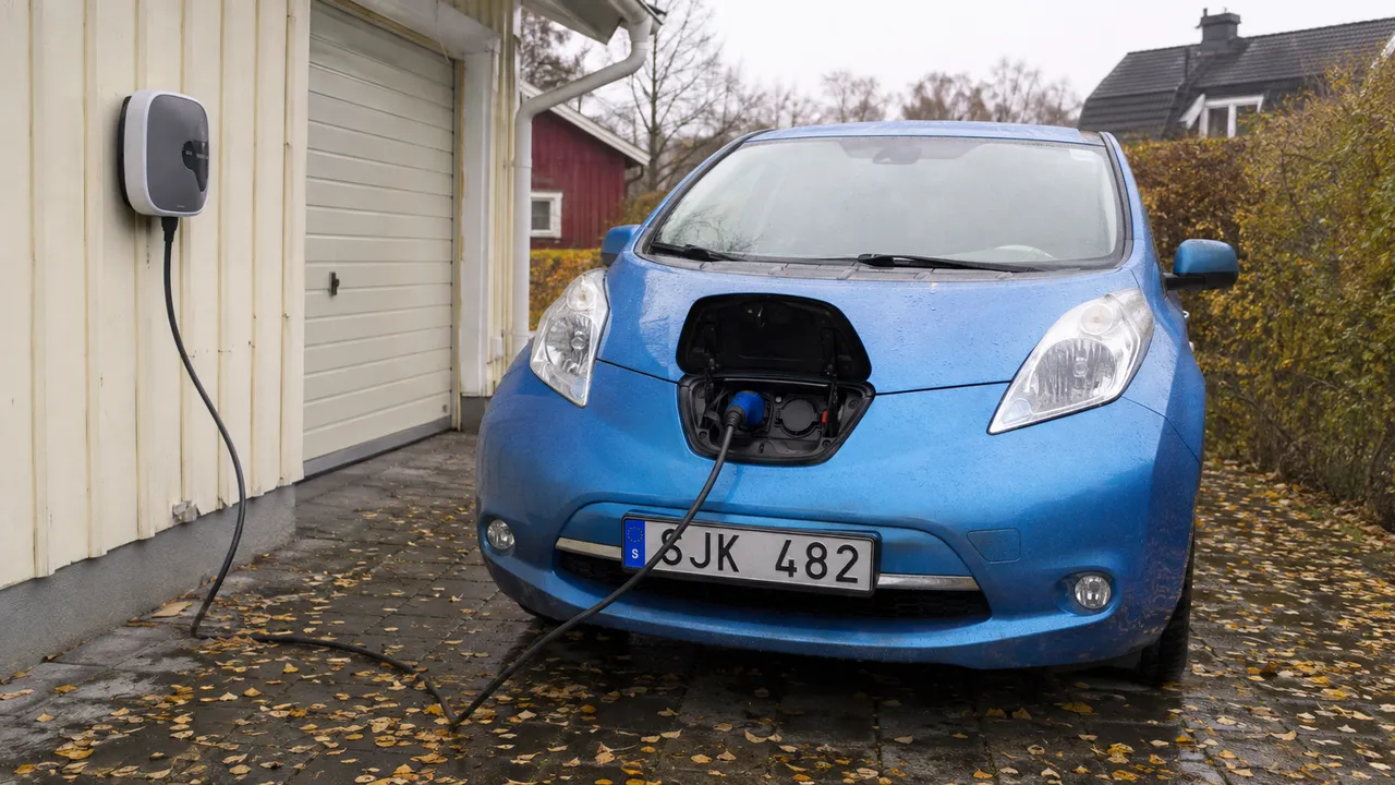 Blå Nissan Leaf med laddkabel ansluten i fronten på en våt villauppfart