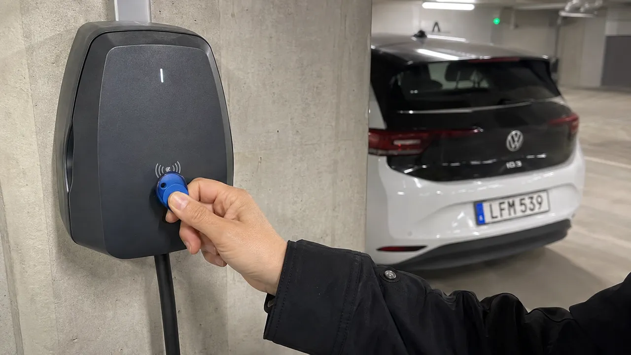 Hand håller en RFID-bricka framför en laddbox i ett parkeringsgarage