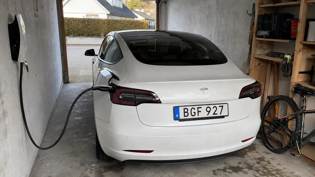 Vit Tesla laddas från en väggladdare i ett villagarage